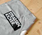 STRASSENKICKER Logo und umgenähter Flap des Fitnesstuchs auf Holzboden