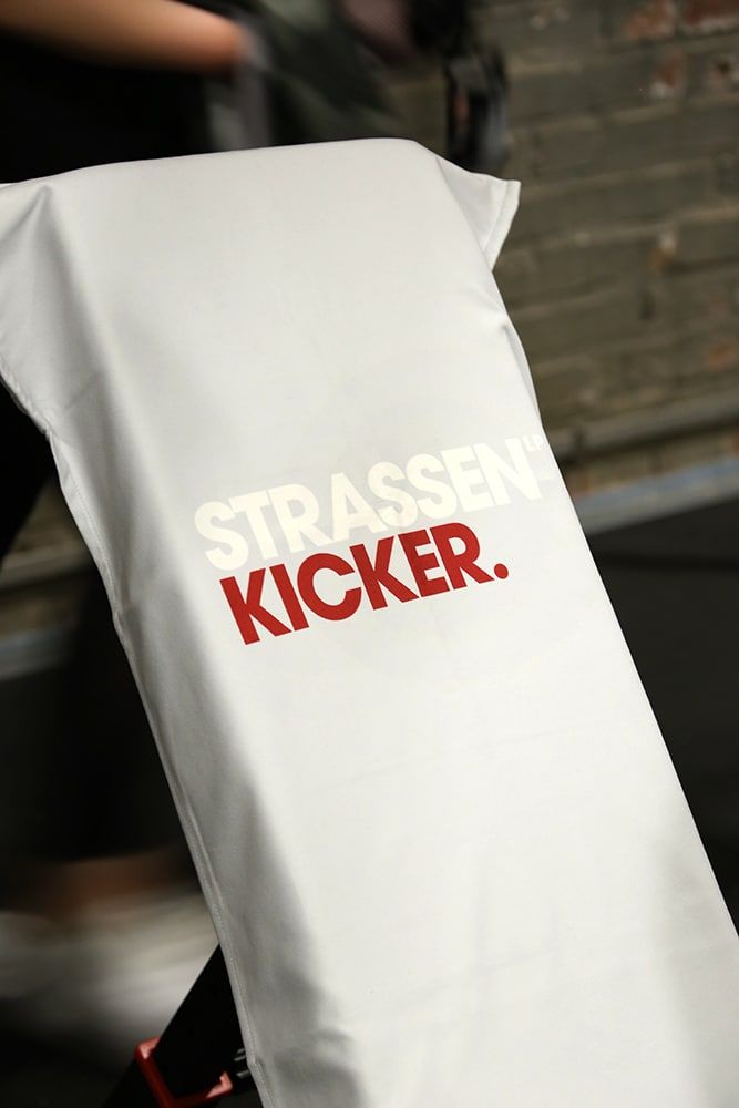 STRASSENKICKER Fitnesstuch ‘Hellgrau’ mit weiß-rotem Schriftzug über einer Hantelbank