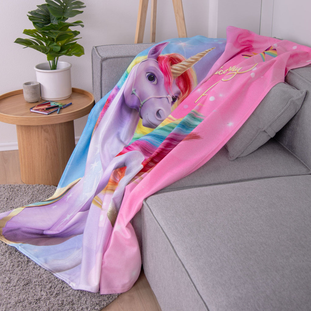 Unicorn Academy Fleecedecke ‘Magic’ auf einem grauen Sofa