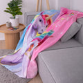 Unicorn Academy Fleecedecke ‘Magic’ auf einem grauen Sofa