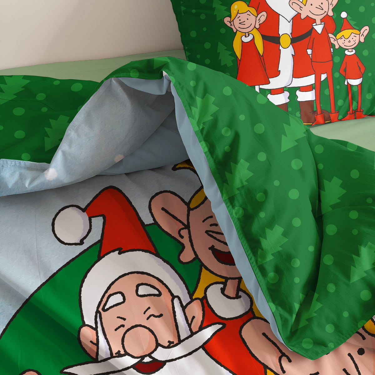 Bettwäsche ‘Nordpol-Helden’ auf dem Bett: der Weihnachtsmann und ein Elf auf dem Bettbezug, die grüne Tannen-Rückseite umgeschlagen, dahinter der Kissenbezug mit dem Weihnachtsmann und drei Elfen