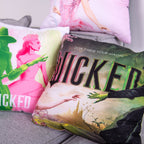 Filmplakat-Kissen mit dem Schriftzug „Wicked“ vor dem Kissen mit den Silhouetten in Grün und Rosa