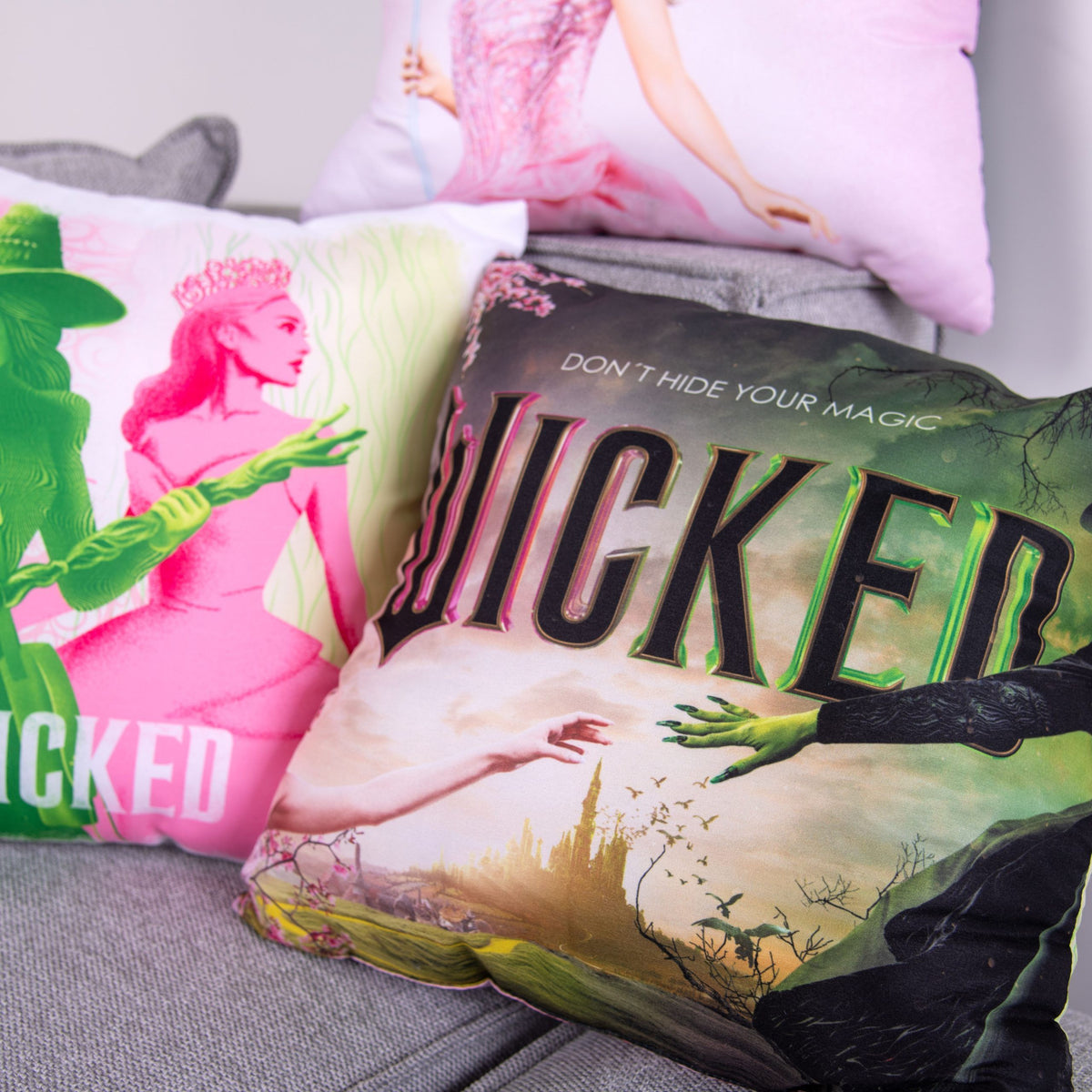 Filmplakat-Kissen mit dem Schriftzug „Wicked“ vor dem Kissen mit den Silhouetten in Grün und Rosa