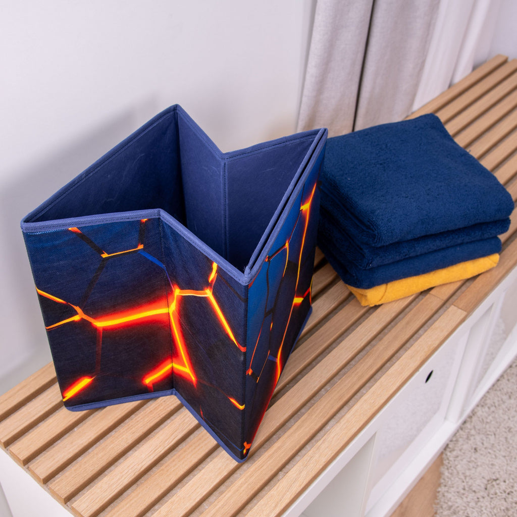 Halb zusammengefaltete Aufbewahrungsbox ‘Lava 3D Effekt’ auf einer Holzbank neben Handtüchern